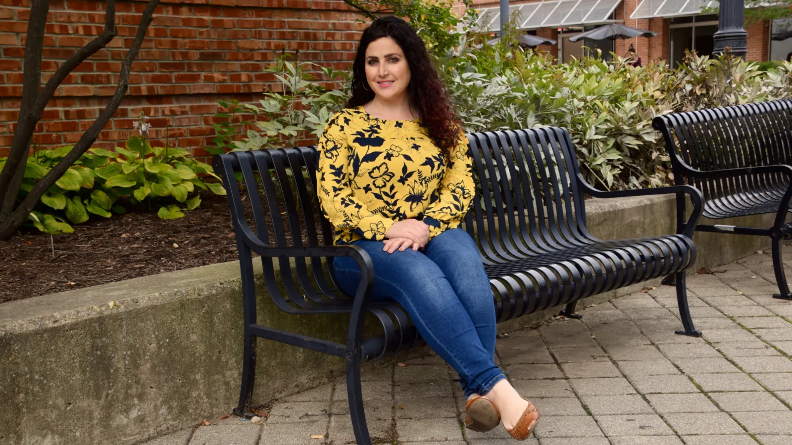 PhD student Ashlee Dauphinais seated on a bench in front of a brick background