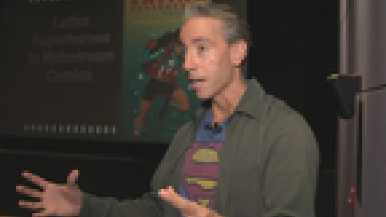 Prof. Aldama speaking in a "Superman" t-shirt. The word "Latinx" and an image of a female superhero are visible behind him. 