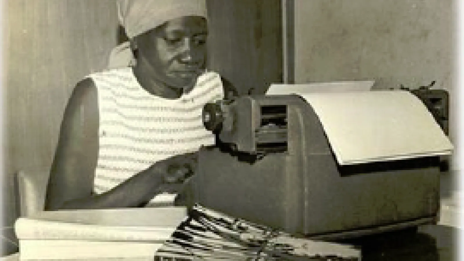 A woman of color seated at a typewriter
