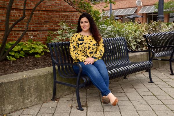 PhD student Ashlee Dauphinais seated on a bench in front of a brick background