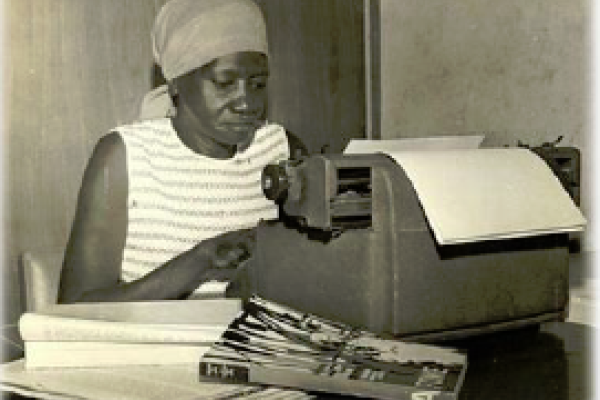 A woman of color seated at a typewriter